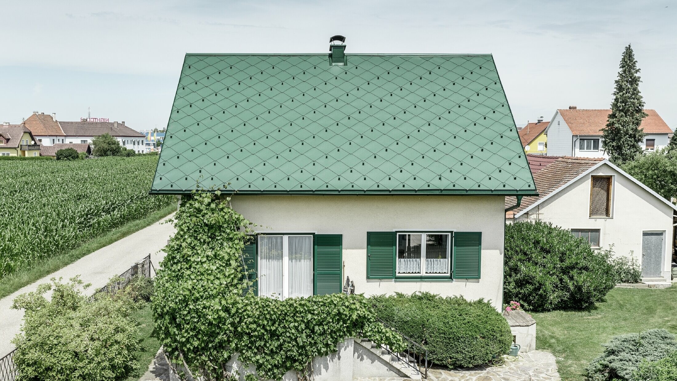 Klassisk enfamilieshus med sadeltag med en taginddækning af aluminium fra mosgrøn med grønne vinduesskodder. Taget blev beklædt med PREFA-tagrombe 44 × 44 i P.10 mosgrøn.