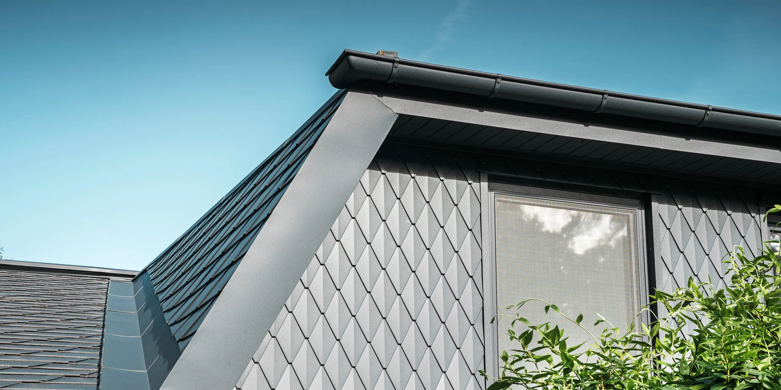 Trapezformet tagvindue på et enfamiliehus i Mechernich, beklædt med små PREFA tagromben i P.10 antracit. Taget er dækket med PREFA tagspån DS.19 i samme farve. Den højkvalitative aluminiumsbeklædning sikrer vejrbestandighed og et moderne, æstetisk udseende.