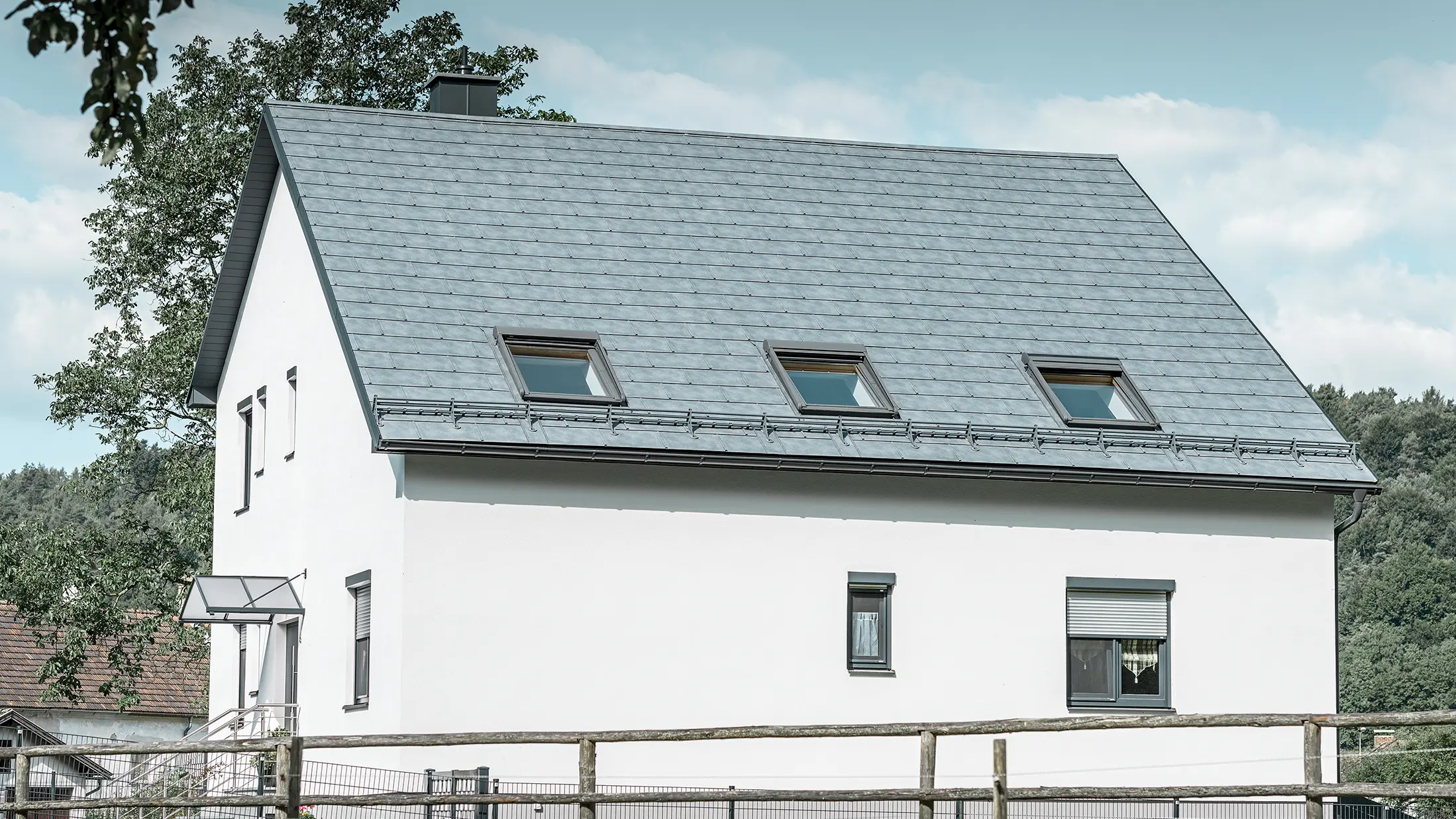 Sadeltaget på det klassiske enfamilieshus er belagt med den nye stengrå PREFA tagplade R.16. Der er indføjet tre tagvinduer i tagfladen og monteret snefang. Facaden er holdt ganske enkelt i hvid.