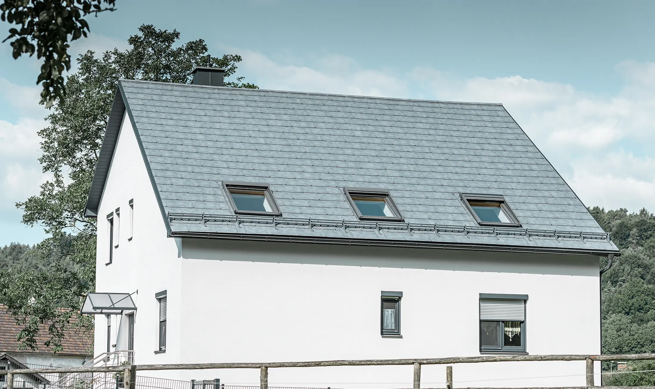 Sadeltaget på det klassiske enfamilieshus er belagt med den nye stengrå PREFA tagplade R.16. Der er indføjet tre tagvinduer i tagfladen og monteret snefang. Facaden er holdt ganske enkelt i hvid.