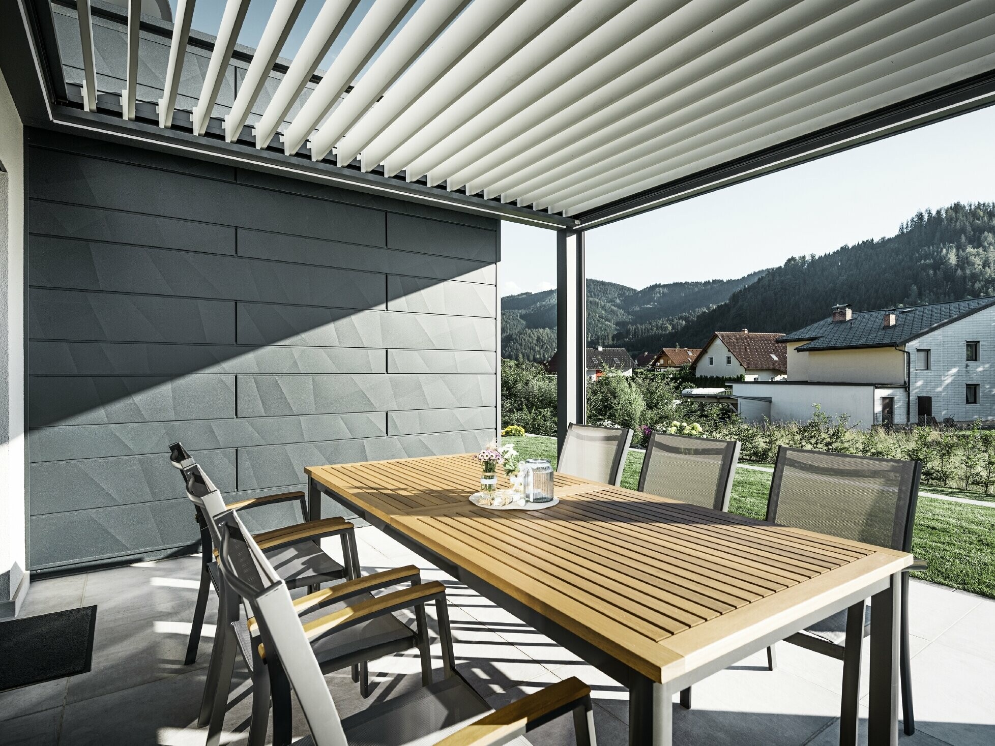 Lameloverdækket beskyttet altan med bord og stole; en facadeside er beklædt med PREFA Siding.X-facadepaneler i antracit.