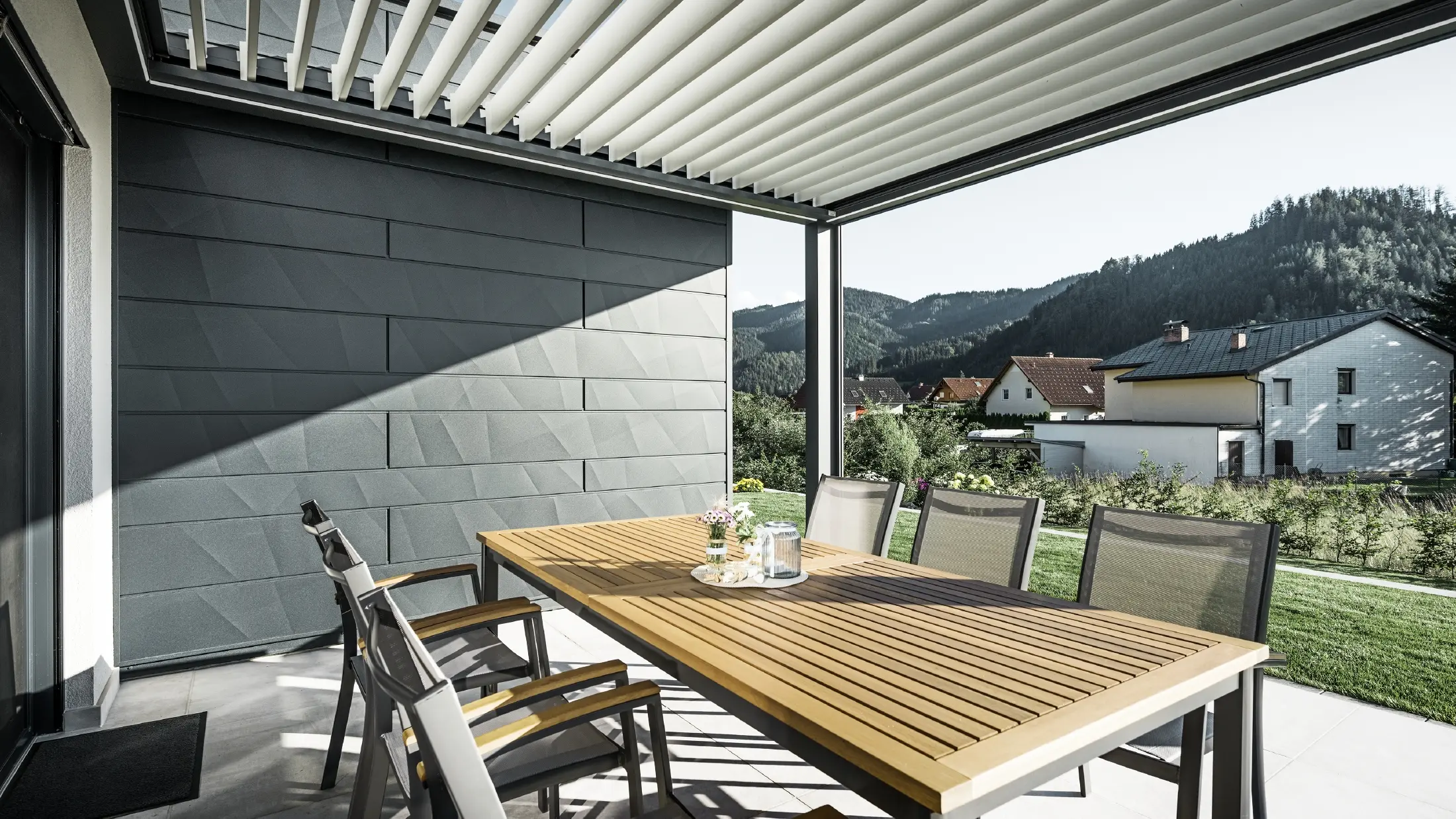 Lameloverdækket beskyttet altan med bord og stole; en facadeside er beklædt med PREFA Siding.X-facadepaneler i antracit.