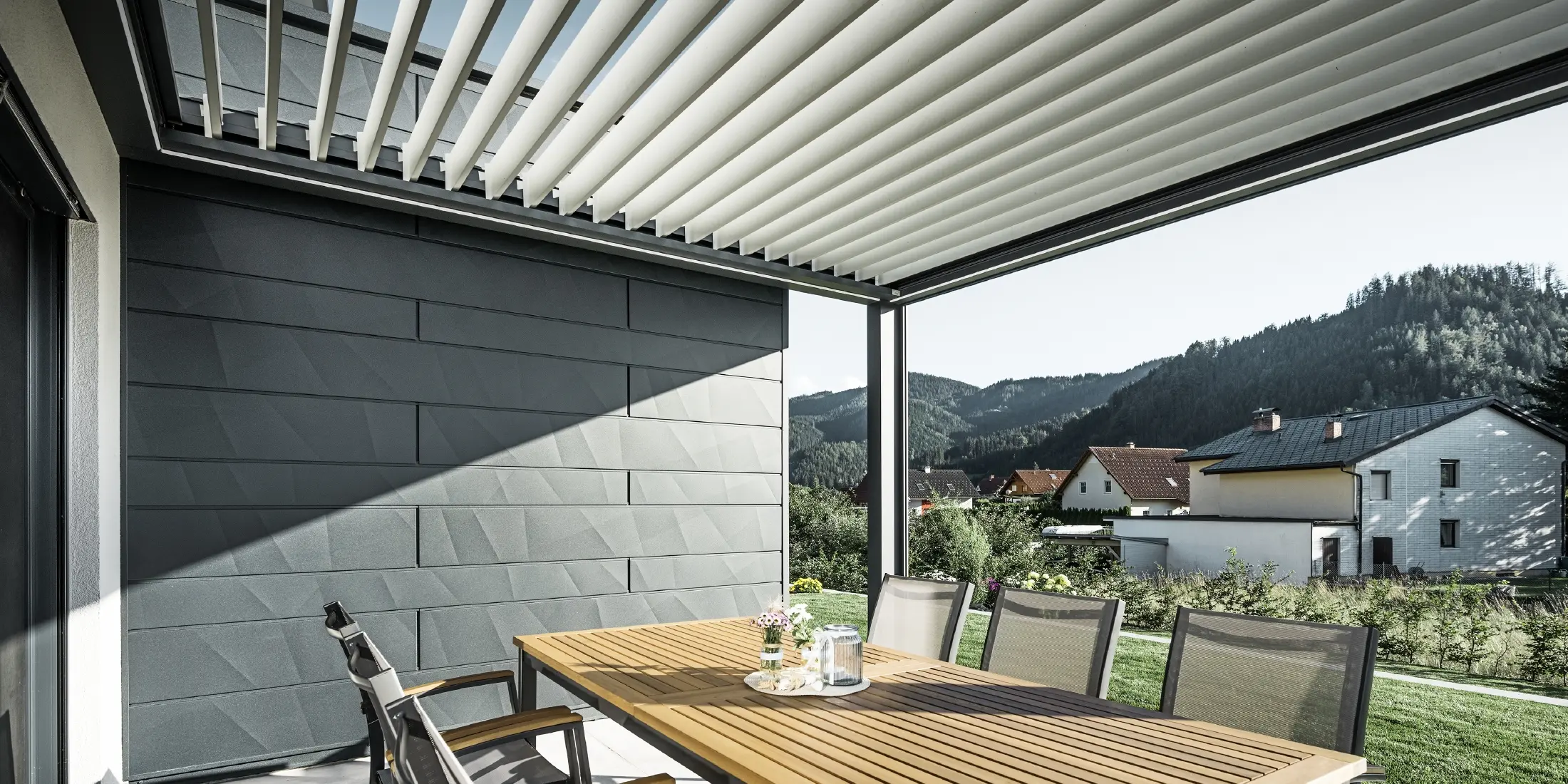 Lameloverdækket beskyttet altan med bord og stole; en facadeside er beklædt med PREFA Siding.X-facadepaneler i antracit.
