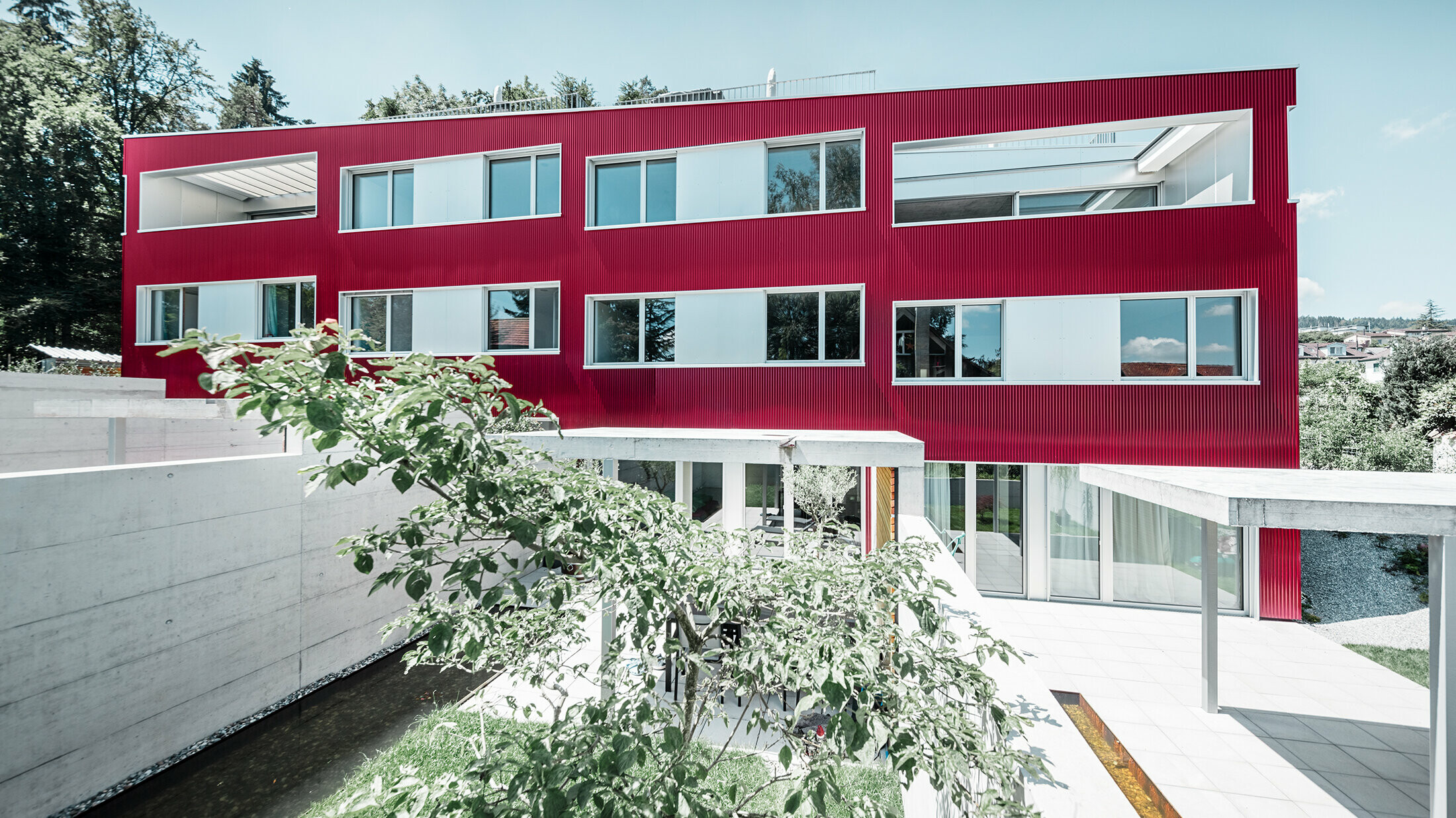 Boligbygning med fladt tag og balkoner med vinrød facade med PREFA-profilbølge 