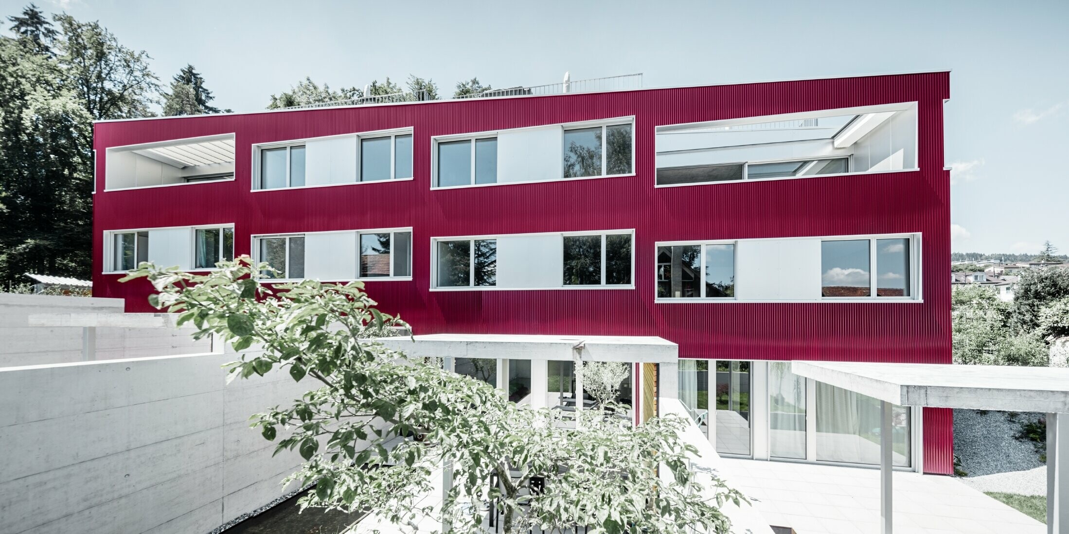 Boligbygning med fladt tag og balkoner med vinrød facade med PREFA-profilbølge 