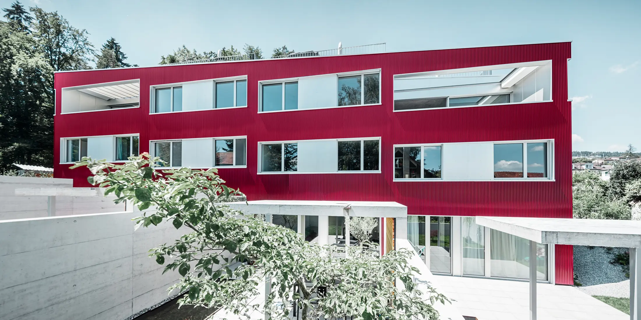 Boligbygning med fladt tag og balkoner med vinrød facade med PREFA-bølge 