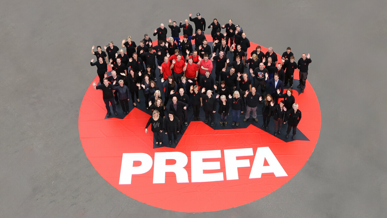 PREFA Team stehend auf einem roten PREFA Logo