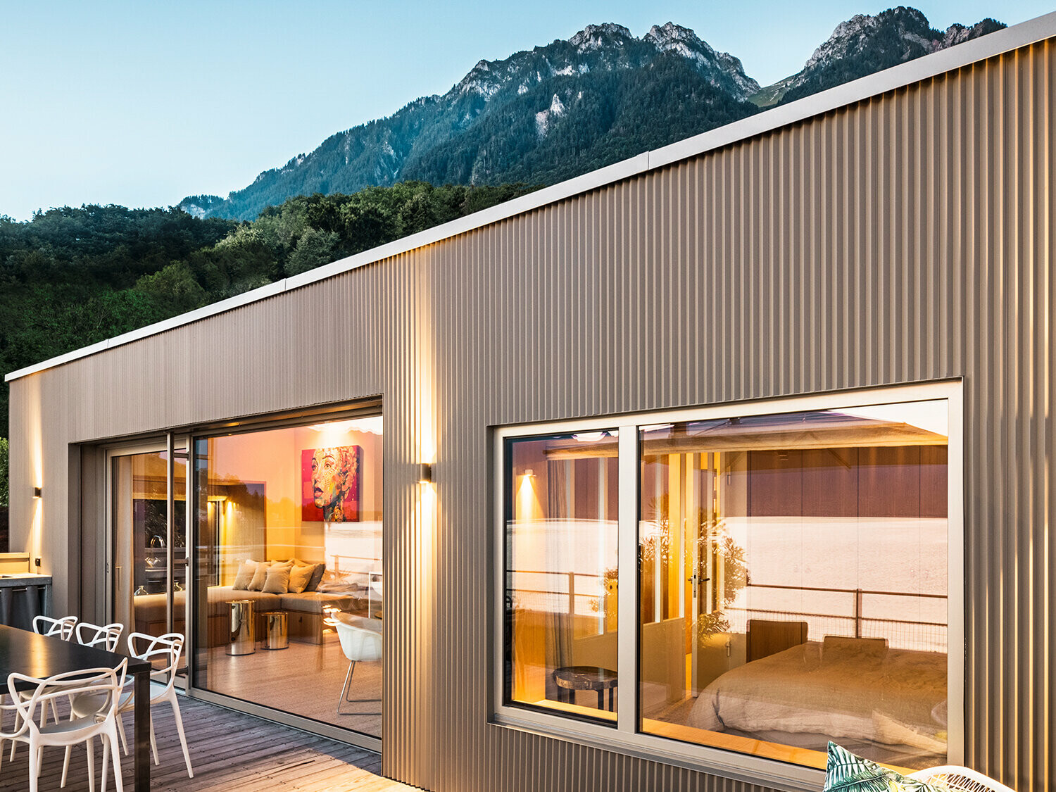 Visning af terrassen og del af bygningens indre om aftenen.