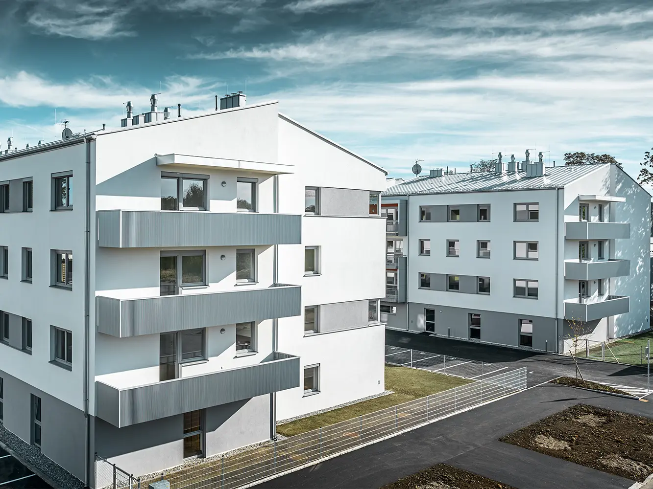 Moderne beboelseshusanlæg med hvid facade og altaner med PREFA-takker i sølvmetallic