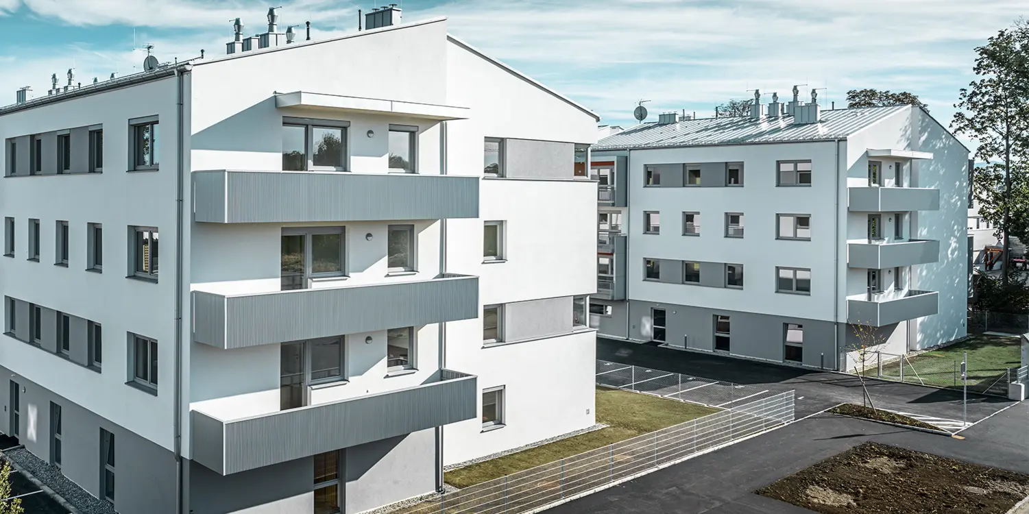 Moderne beboelseshusanlæg med hvid facade og altaner med PREFA-takker i sølvmetallic