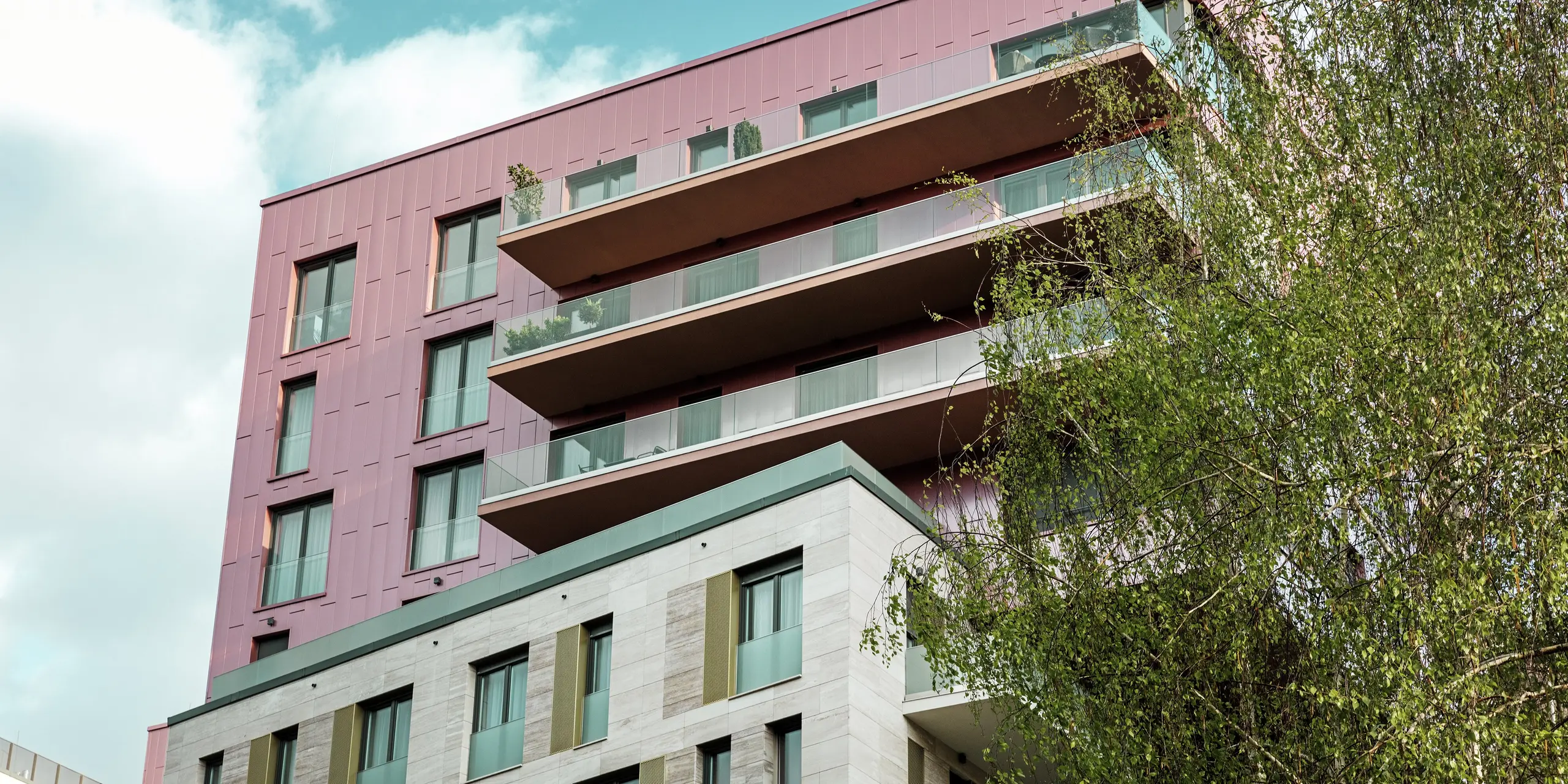 Oberer Gebäudeteil des Wohnkomplexes „Grand Corvin“ in Budapest mit markanter PREFA Siding Aluminiumfassade in vertikaler Verlegung und Sonderfarbe Lachsmetallic, gebürstet. Die hochwertigen Fassadenpaneele verleihen dem Gebäude ein modernes, elegantes Erscheinungsbild und setzen einen auffälligen architektonischen Akzent im revitalisierten Corvin-Viertel.