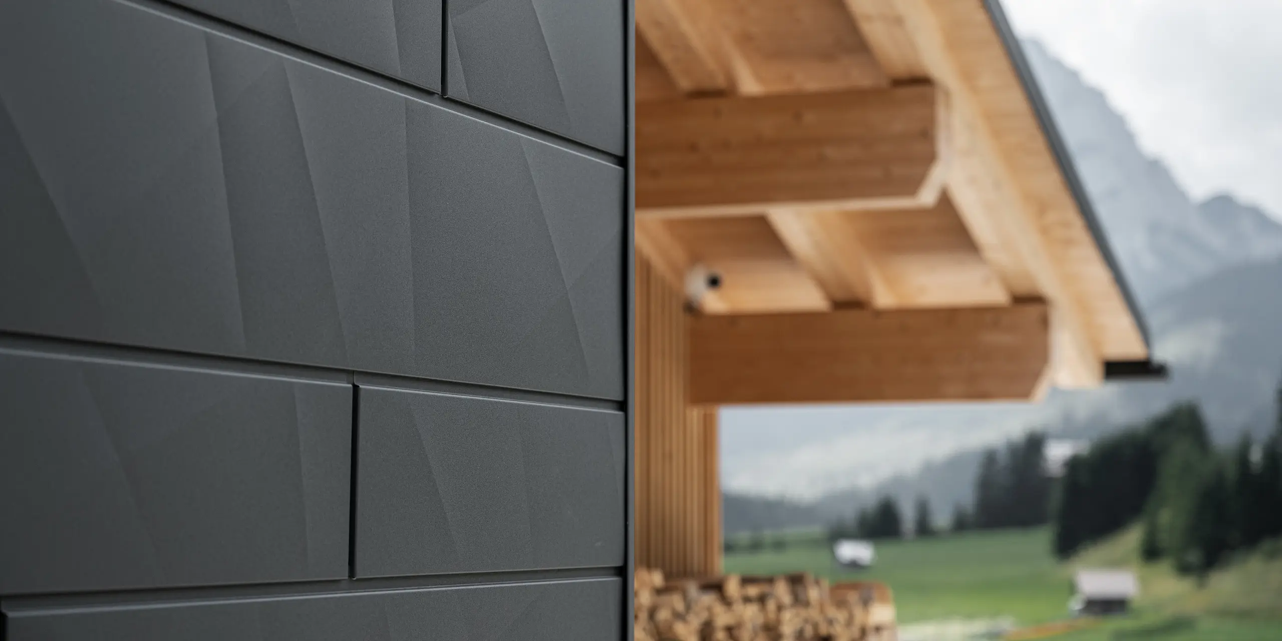 Nærbillede af Siding.X-facadepaneler i P.10 sort fra PREFA på Casa Hoffe i Sappada, Italien. Facadesystemet af aluminium er anbragt omhyggeligt i et moderne, abstrakt design, der giver en tilsvarende kontrast til de synlige træelementer i tagkonstruktionen. Den nyskabende facadeløsning føjer sig harmonisk ind i det alpine miljø og repræsenterer forbindelsen mellem funktioner, bestandighed og æstetisk byggekultur.