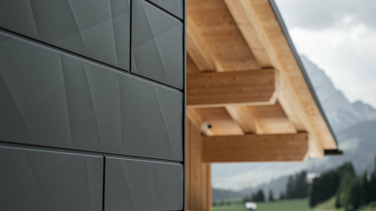 Nærbillede af Siding.X facadeplader i P.10 sort fra PREFA på Casa Hoffe i Sappada, Italien. Facadesystemet i aluminium er monteret i et moderne, abstrakt design, der danner en flot kontrast til de synlige træelementer i tagkonstruktionen. Den innovative facadeløsning passer perfekt ind i det alpine miljø og står for en kombination af funktionalitet, holdbarhed og æstetisk byggekultur.