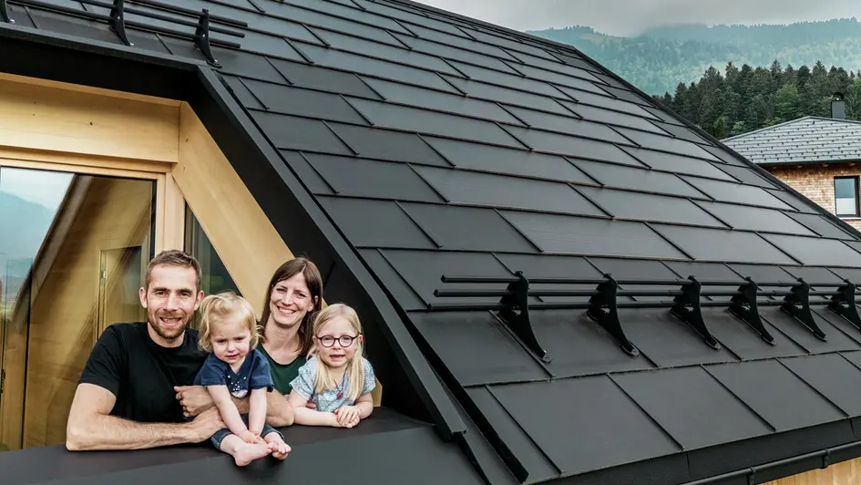 De to bygherrer nyder sammen med deres børn udsigten fra loggiaen i deres nybyggede hus, der er udstyret med stilfulde PREFA-solcelletagplader i P.10 sort.