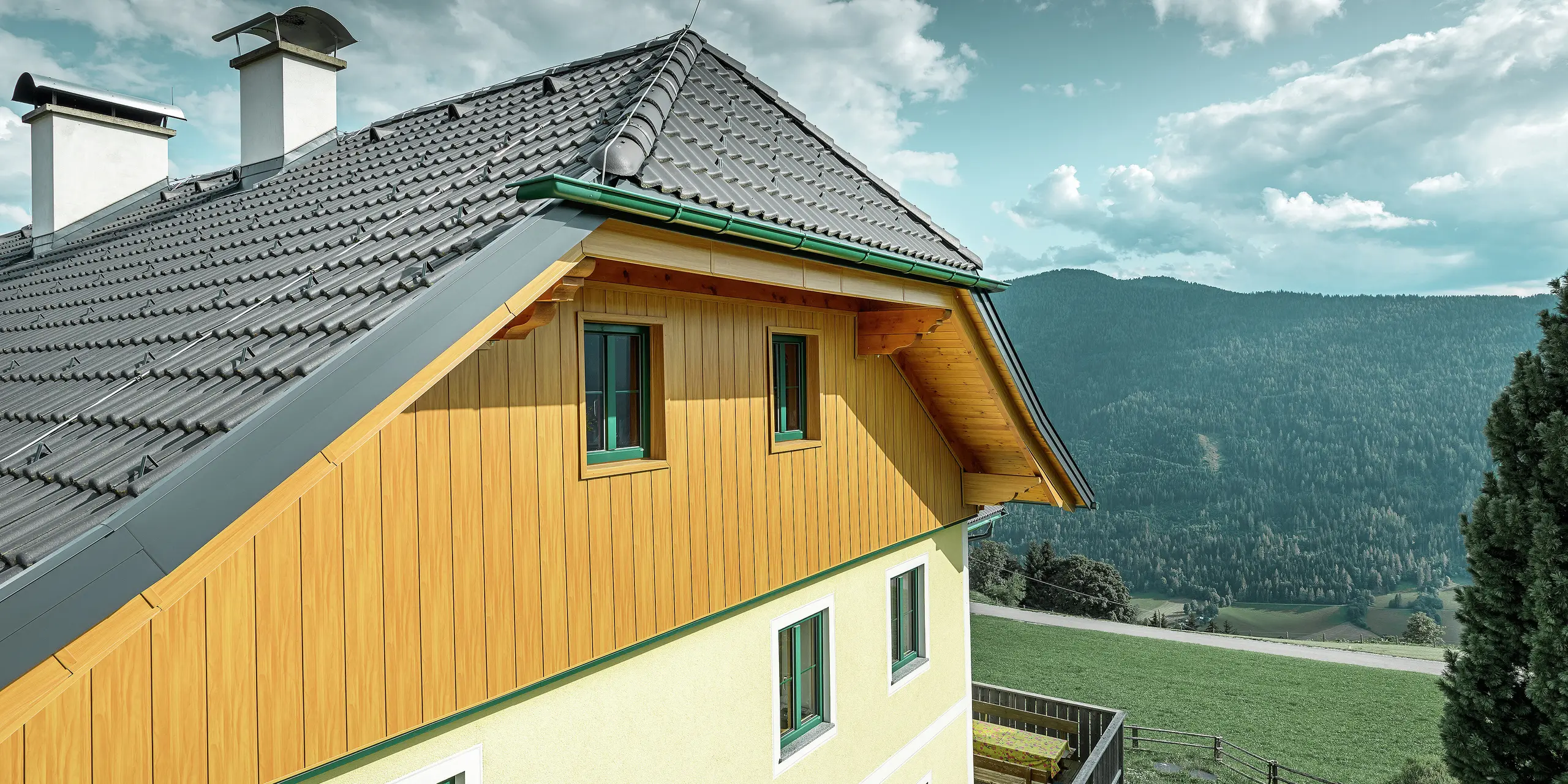 Detailansicht der Giebelverkleidung mit PREFA Sidings in Eiche natur an einem Wohnhaus in Ranten mit Blick auf die umliegende Berglandschaft.