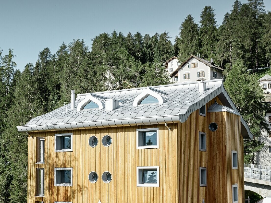 Boliganlæg i St. Moritz med træfacade og aluminiumtag med svunget tagrende i sølvmetallic