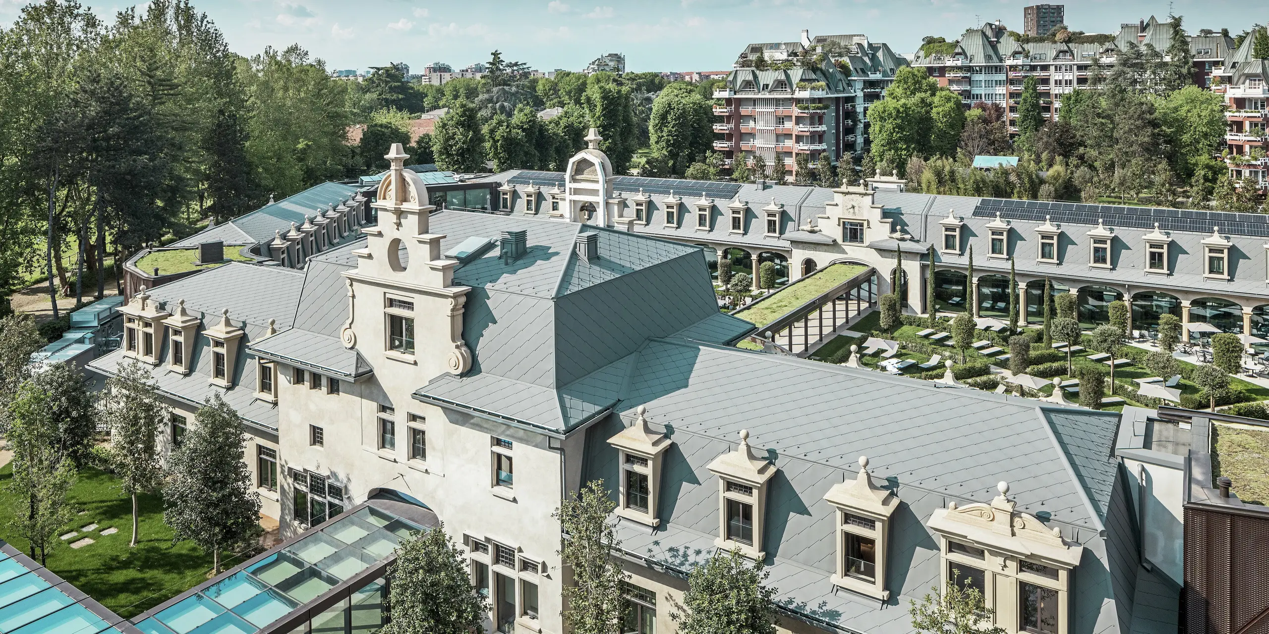 Samlet billede af det imponerende anlæg »De Montel – Terme Milano« med fredet jugendstilarkitektur og moderne wellness-atmosfære. Den store tagdækning med PREFA tagrombe 44 × 44 i P.10 lys grå giver komplekset en elegant ensartethed. Integrerede PV-moduler, grønne tage og glasforbindelser mellem bygningerne afspejler kravene til bæredygtighed og moderne design i en urban kontekst.