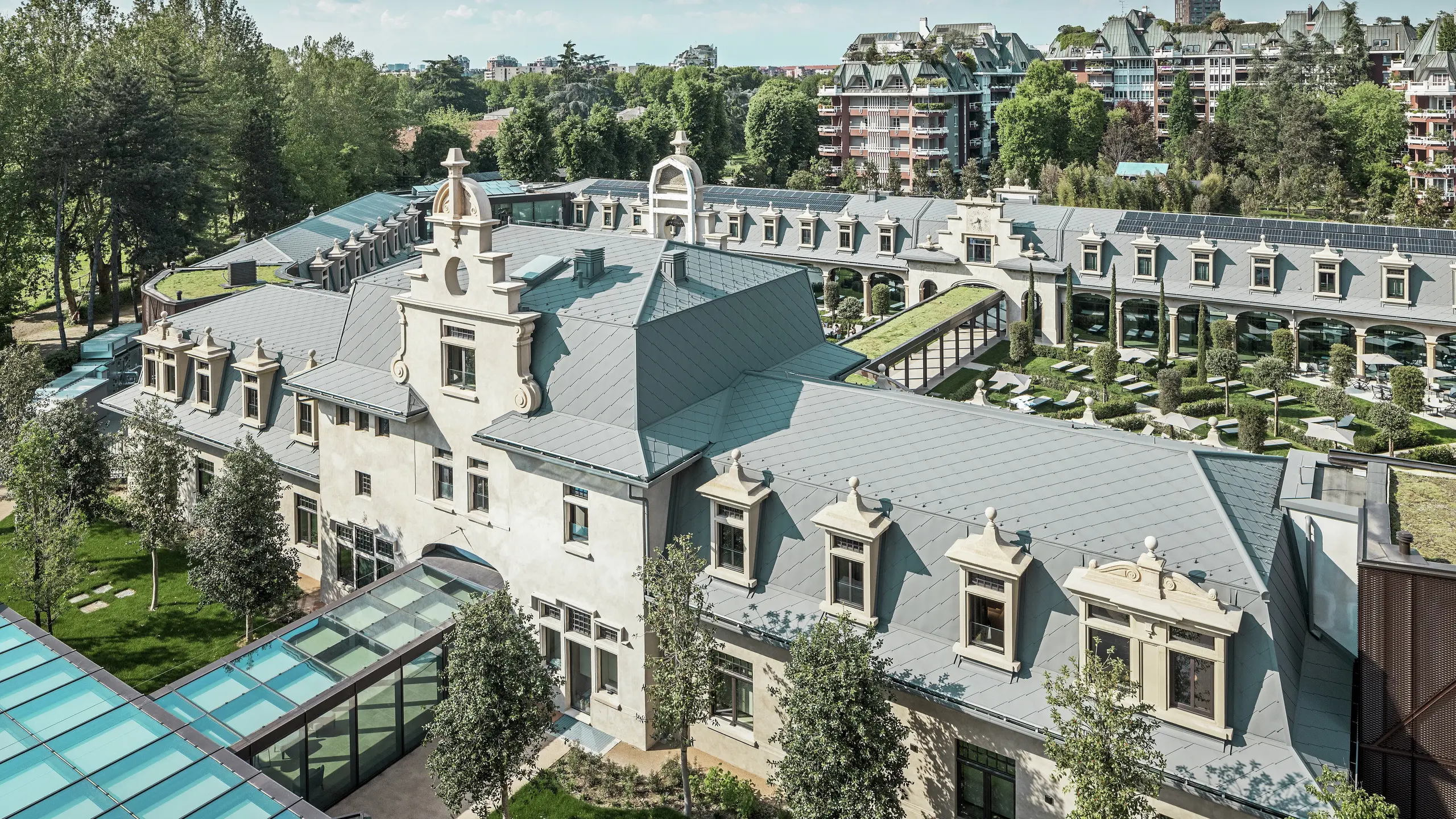 Samlet billede af det imponerende anlæg »De Montel – Terme Milano« med fredet jugendstilarkitektur og moderne wellness-atmosfære. Den store tagdækning med PREFA tagrombe 44 × 44 i P.10 lys grå giver komplekset en elegant ensartethed. Integrerede PV-moduler, grønne tage og glasforbindelser mellem bygningerne afspejler kravene til bæredygtighed og moderne design i en urban kontekst.