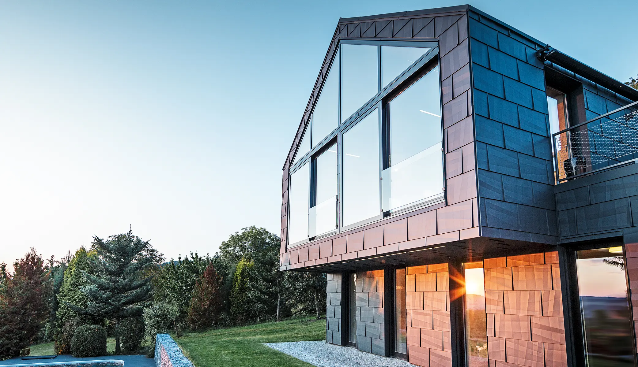 Moderne parcelhus uden tagudhæng med store vinduer og FX.12-facade i antracit, fotograferet ved solnedgang.