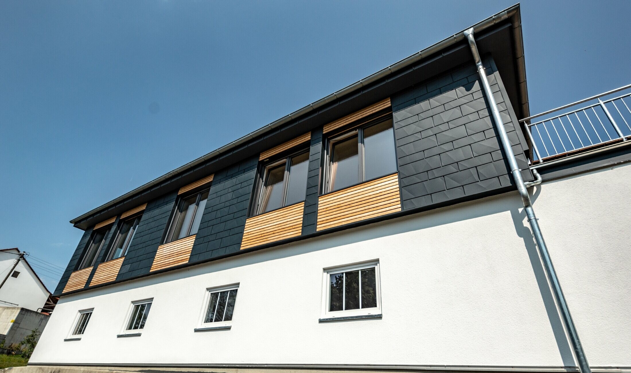 Facadedesign udført i forskellige byggematerialer: der er anvendt PREFA Siding.X i aluminium i antracit, en vandret træfacade og en hvid pudset facade.