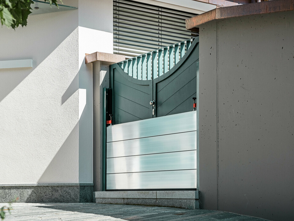 Nahaufnahme eines montierten PREFA Hochwasserschutzsystems am Gartentor eines Einfamilienhauses in Schwaz, Tirol. Die eingesetzten Dammbalken aus Aluminium sind in seitlich angebrachte Befestigungsprofile eingeschoben und schützen den Eingangsbereich zuverlässig vor eindringendem Wasser. Das System überzeugt durch seine schlichte Optik, die schnelle Einsatzbereitschaft und die korrosionsbeständigen Materialien - ideal für den privaten Objektschutz. Die Wandprofile sind in der gleichen Farbe wie die Tür gehalten, so dass ein harmonischer Gesamteindruck entsteht.
