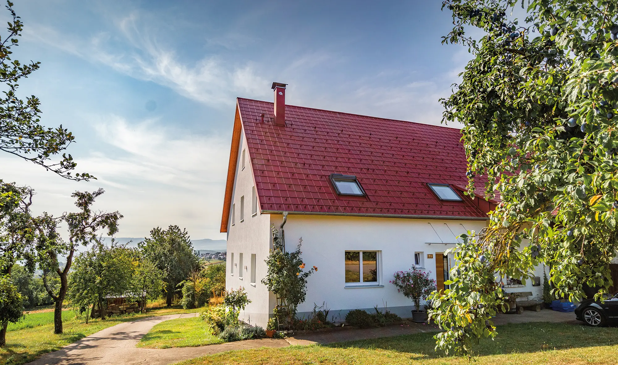 Romantisk lille hus på landet med mange træer og buske. Belagt med et PREFA-tag i oxidrød.