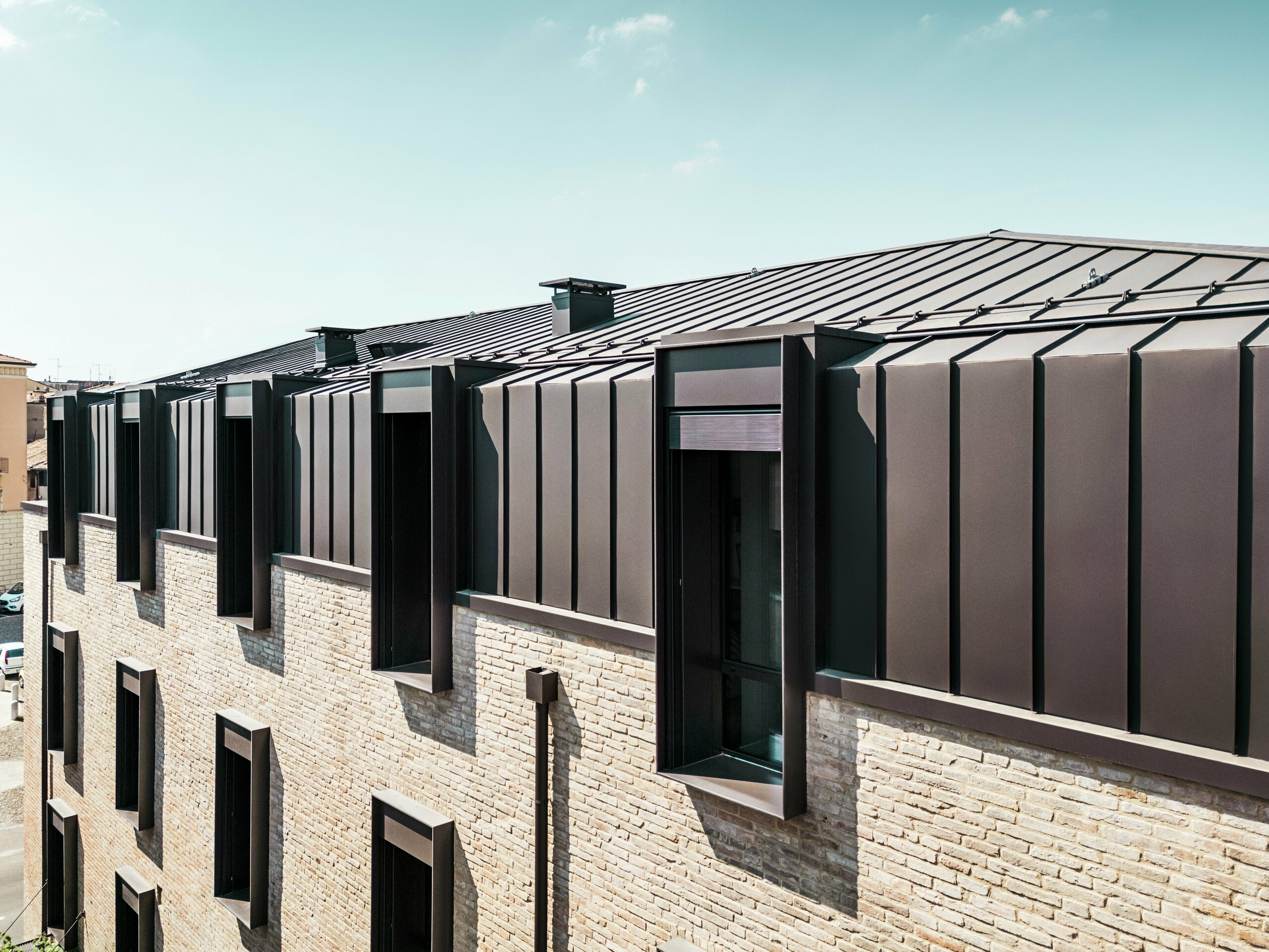 Moderan dizajn krova i fasade kuće od opeke u Italiji s PREFALZ aluminijskim krovom u boji P.10 smeđa lješnjaka i upečatljivim krovnim prozorima (zabatima).