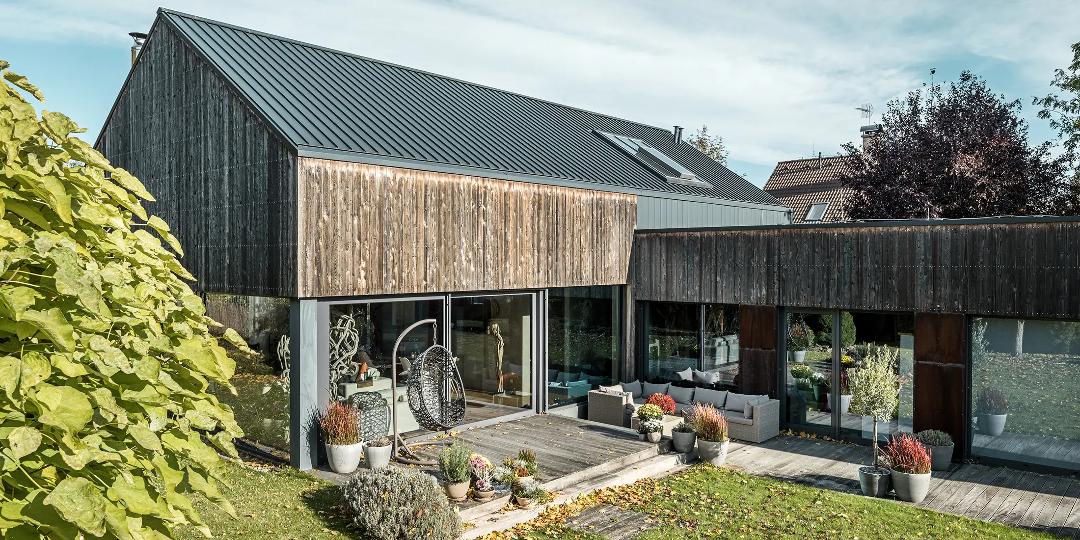 Enfamilieshus med sadeltag, beklædt med dobbeltstående fals PREFALZ i antracit og forvitret træfacade. Med flot træterrasse og store vinduesflader i stueetagen.