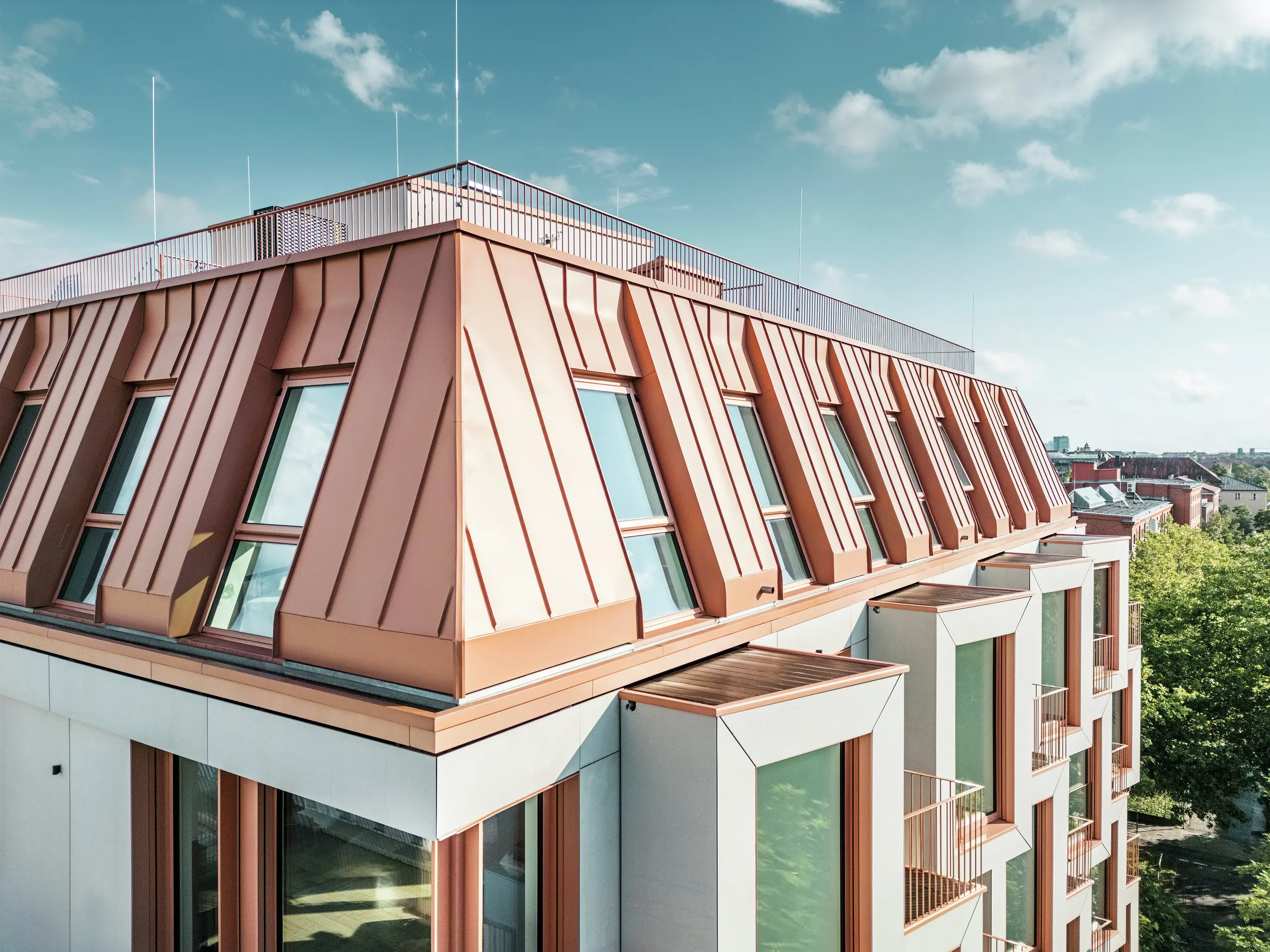 Detailansicht der markanten PREFALZ-Dachdeckung des Wohngebäudes Van B in München. Das farblich abgestimmte Aluminiumdach besticht durch seine hochwertige Verarbeitung, außergewöhnliche Langlebigkeit und Witterungsbeständigkeit. Die schrägen Fenster und die klar strukturierten Fassadenelemente runden das innovative Designkonzept ab. Ideal für moderne Architektur, in der Funktionalität und Ästhetik im urbanen Leben Hand in Hand gehen. Am unteren Bildrand sind Reihen von Erkerfenstern zu erkennen.