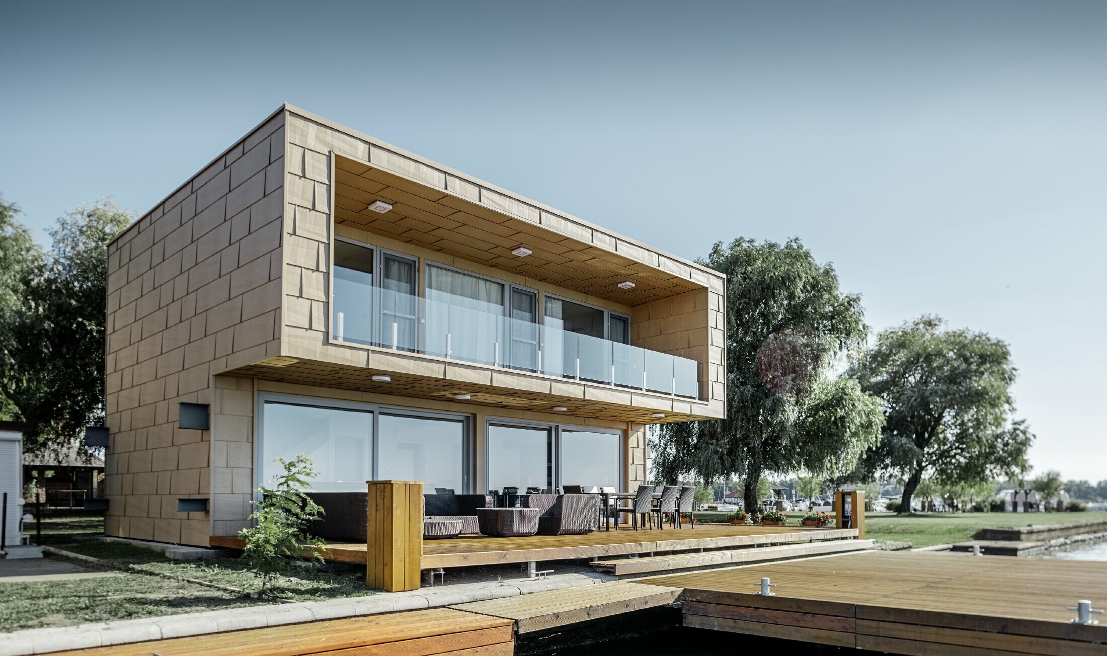 Moderne weekendhus med fladt tag og store vinduesflader ved havet med en vinklet aluminiumfacade i sandbrun