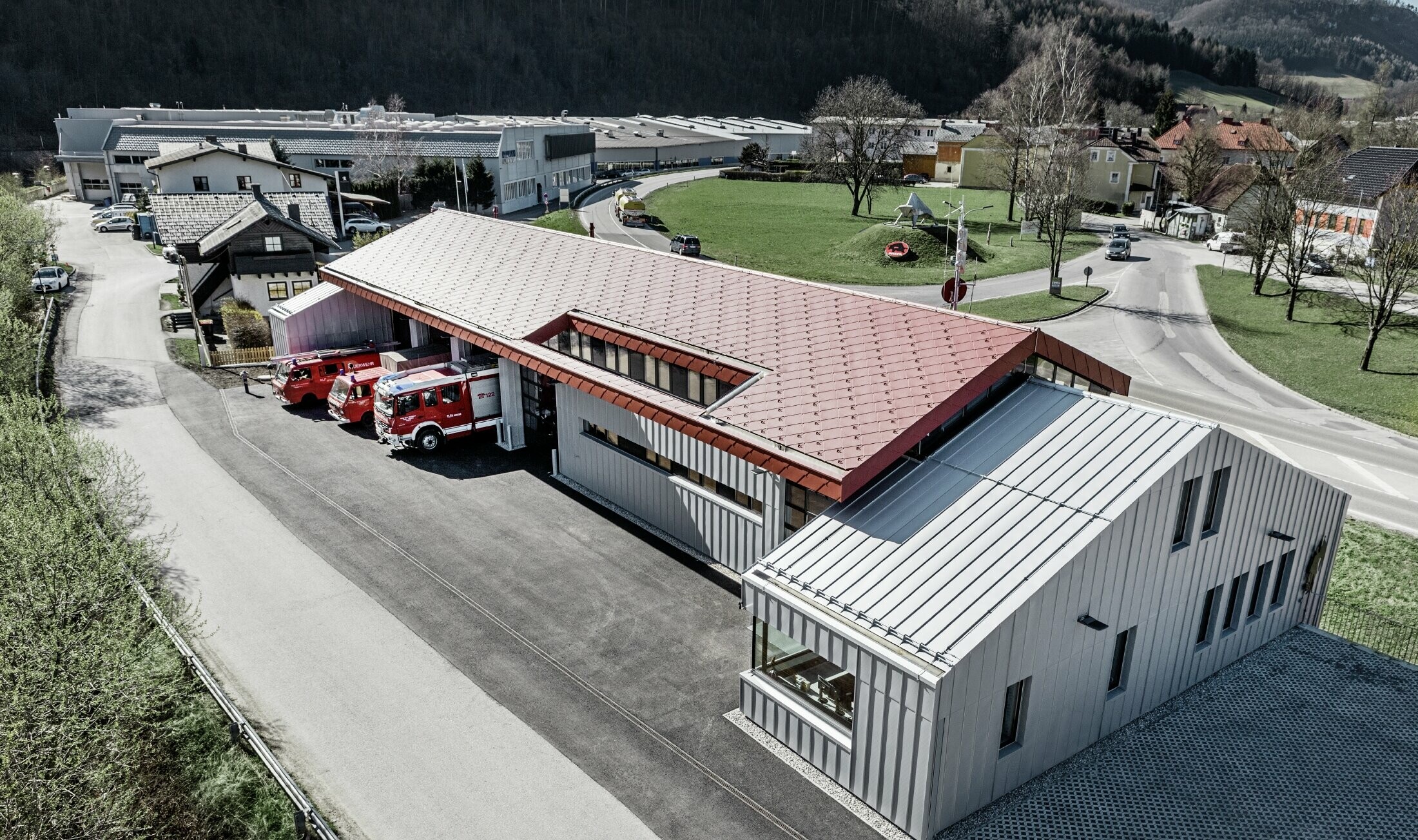 Billede af virksomhedsbrandvæsenet i Marktl/Lilienfeld i fugleperspektiv. Den venstre side af bygningen er på taget og facaden fuldt belagt/beklædt med rombe 44 i oxidrød. Den højre side får en aluminiuminddækning med Prefalz i sølvmetallic.