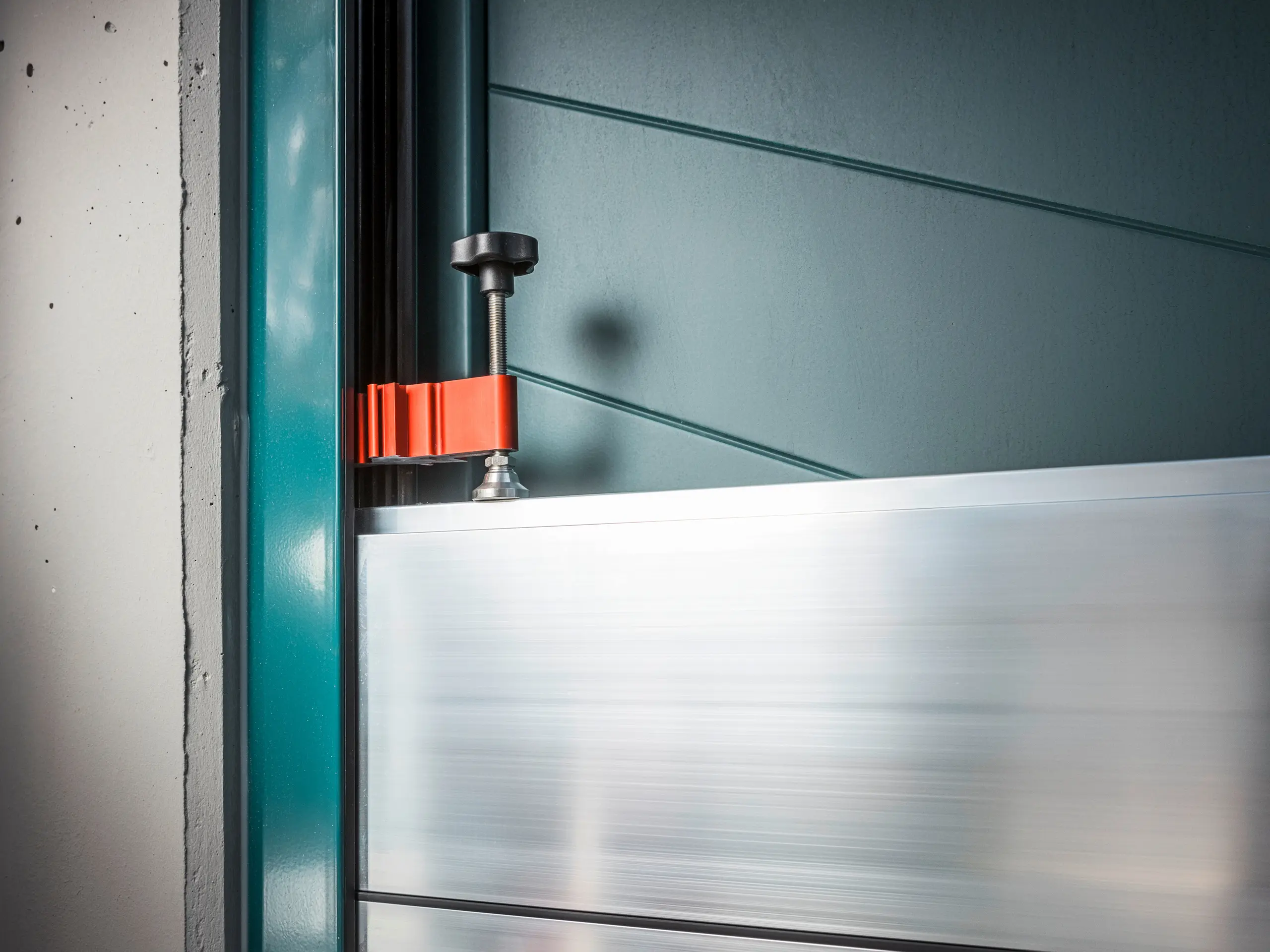 Nærbillede af PREFA-oversvømmelsessikringssystemet på en portramme, der består af dæmningsbjælker i aluminium, som er fastgjort med en robust, rød klemme (klemmestykket) for at sikre en sikker beskyttelse mod oversvømmelse.