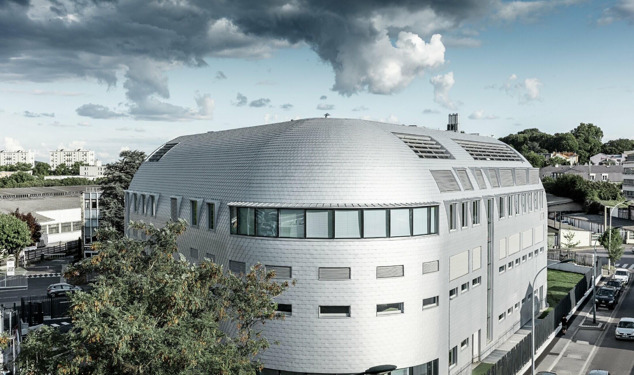 Virksomhedsbygning med rund kuppel og belagt med PREFA aluminiumtagspåner i sølvmetallic.
