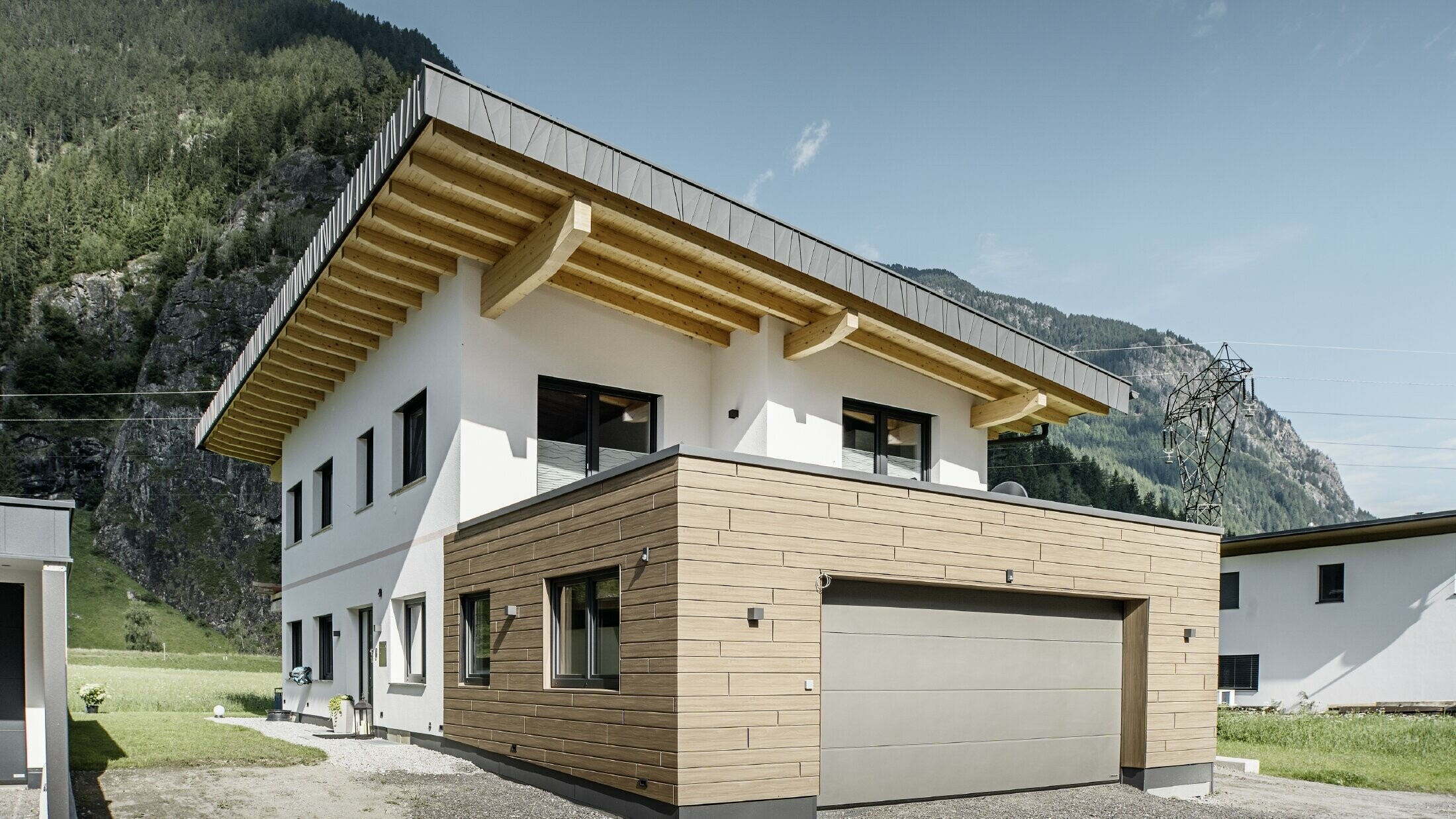 Moderne enfamiliehus med renoveret facade: nyudført udvendig facade med horisontal facadebeklædning i trælook, kombineret med hvidpudsede flader, integreret garagebeklædning og moderne arkitektur i alpine omgivelser.
