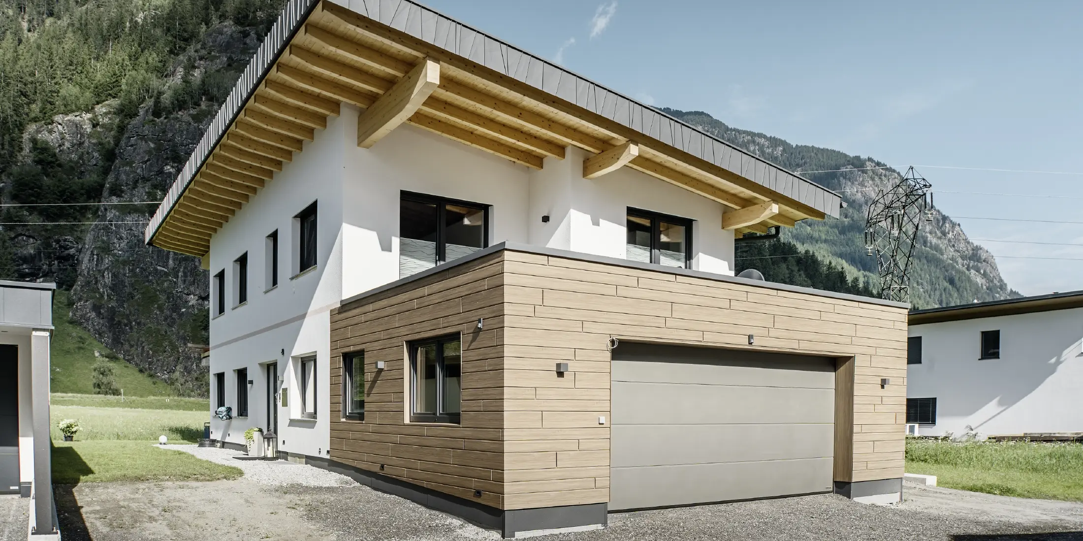 Moderne enfamiliehus med renoveret facade: nyudført udvendig facade med horisontal facadebeklædning i trælook, kombineret med hvidpudsede flader, integreret garagebeklædning og moderne arkitektur i alpine omgivelser.