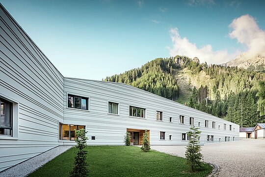 Aluminij susreće preciznost – harmoničan dijalog između tehnologije i prirode. Pred impresivnom kulisom Dolomita, „Villaggio Alpino Tempesti“ predstavlja se jasnim linijama i modernim dizajnom. Fasada od PREFALZ-a u boji P.10 Prefaweiß nije samo iznimno otporna, već zahvaljujući svojoj svijetloj boji stvara i ugodnu mikroklimu reflektirajući sunčeve zrake. Zelene površine i drveni elementi na ulazu u vojni objekt stvaraju iznenađujuće gostoljubivu atmosferu.