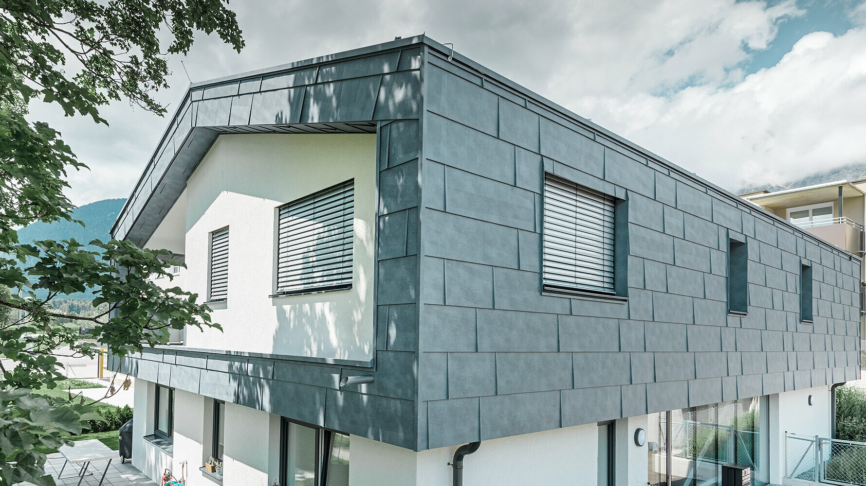 Moderne parcelhus uden tagudhæng: Den øverste etage er beklædt med PREFA facadepaneler FX.12 i stengrå, og resten er pudset hvidt.