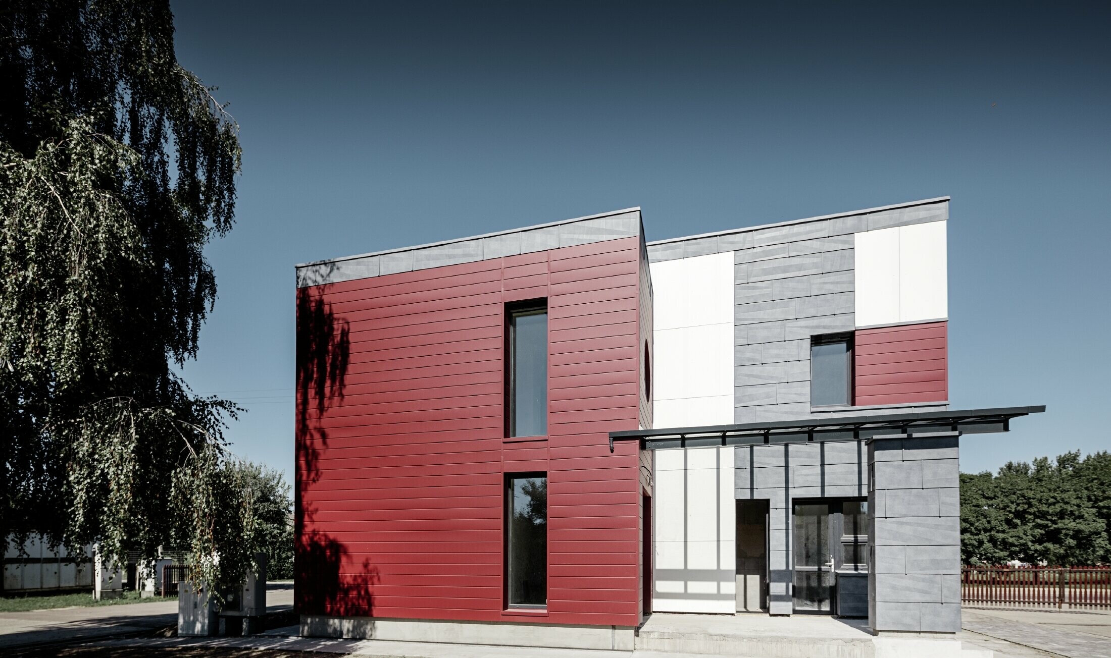 Moderne kontorbygning med en delt facade i rød, stengrå og hvid med aluminiumprodukter Sidings, facadepanel FX.12 og aluminiumskompositplade fra PREFA