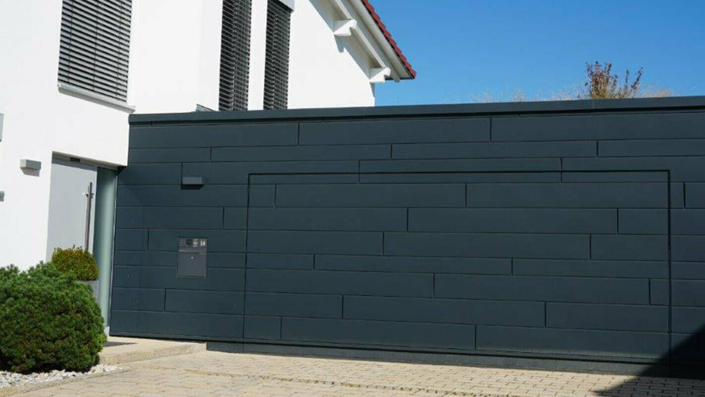 Garagefacade efter renovering med PREFA sidings i antracit, garageporten er monteret på linje med facaden