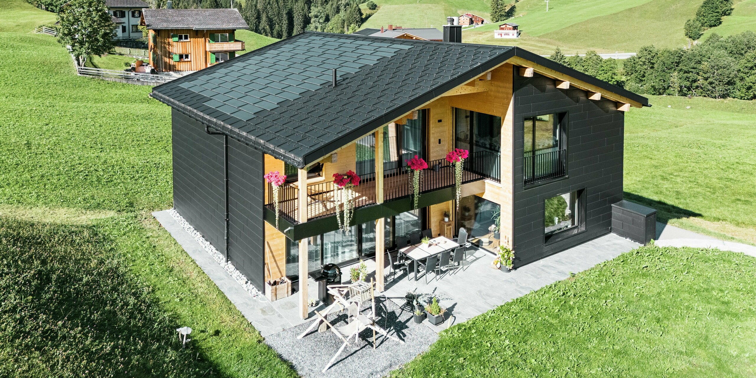 Det elegante parcelhus i de bakkede omgivelser i Ascharina (Schweiz) viser, hvordan aluminium og træ kan kombineres perfekt. De robuste PREFA Siding.X-facadepaneler i P.10 sort harmonerer med taget, der består af PREFA solcelletagpaneler og R.16-tagpaneler i samme farve. Den holdbare aluminiumsbeklædning beskytter bygningen pålideligt mod udfordringerne i det alpine klima.