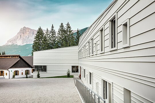 Čisto svjetlo, oštre linije: Fasada vojarne „Tempesti“ u Južnom Tirolu dojmljivo pokazuje kako se moderan dizajn može uklopiti u planinski krajolik. Horizontalne PREFALZ trake u boji P.10 Prefaweiß reflektiraju sunčevu svjetlost, poboljšavaju mikroklimu i oduševljavaju svojom robusnom, dugotrajnom kvalitetom. One su snažan primjer promišljene vojne arhitekture s aluminijem.