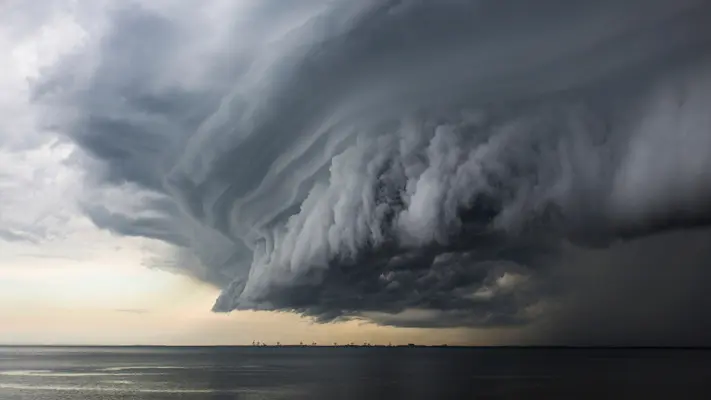 Dramatische, dunkle Unwetterwolken ziehen über eine Stadt auf, symbolisieren drohende Stürme und Gewitter. Mit PREFA Dach- und Fassadensystemen ist Ihr Zuhause zuverlässig vor Unwettern geschützt.