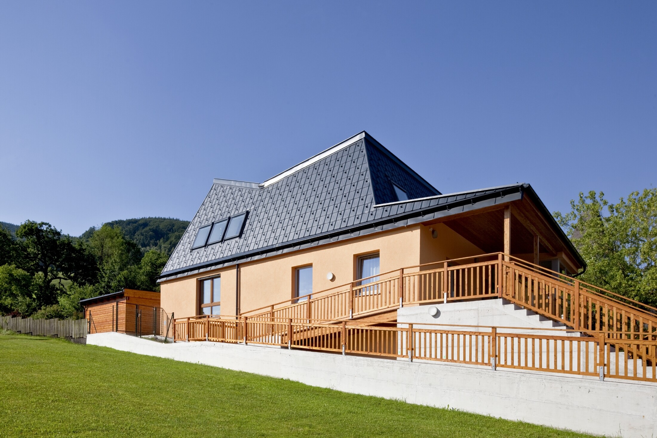Kindergarten mit oranger Putzfassade und verwinkeltem Dach, gedeckt mit der PREFA Dachplatte in P.10 Anthrazit;