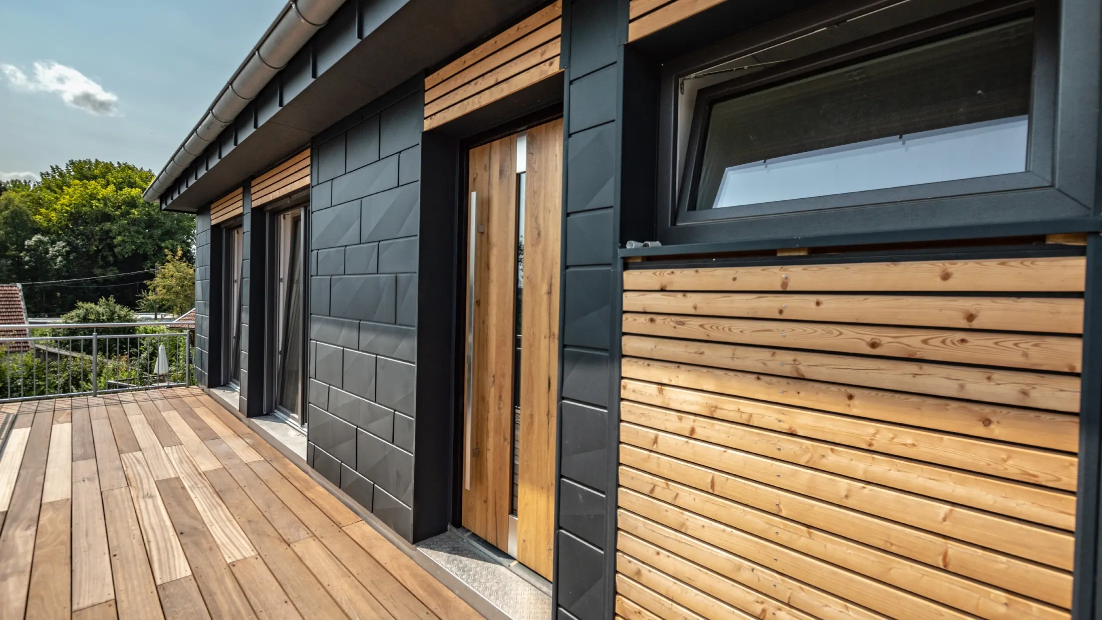 Facadedesign med en blanding af materialerne aluminium - PREFA Siding.X i antracit - og vandrette trælameller.