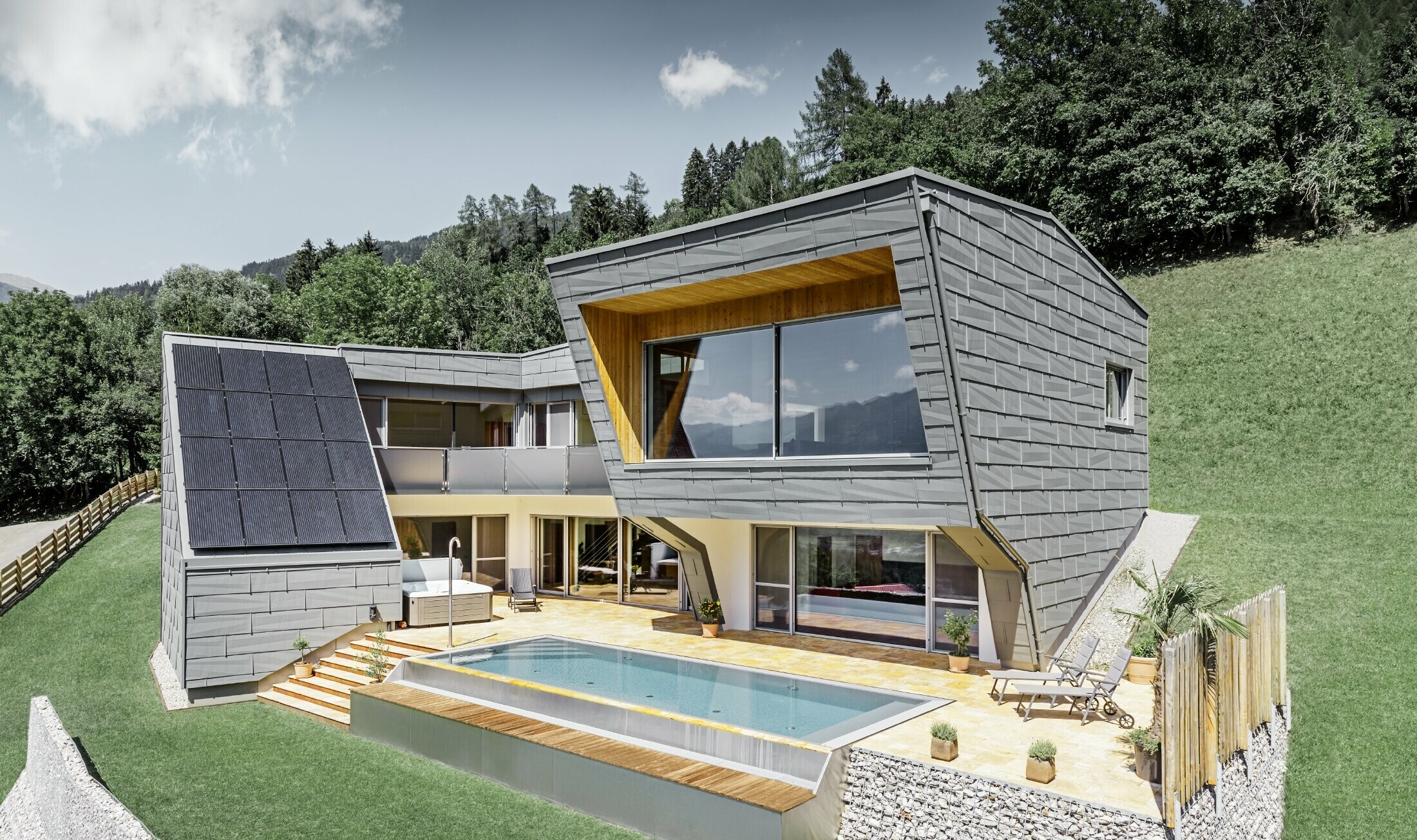 Moderne enfamilieshus på bjergskråning med swimmingpool er beklædt med facadepanel FX.12 fra PREFA i P.10 lysegrå.