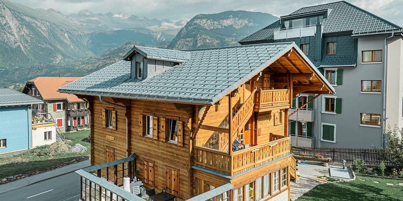 Traditionelt schweizisk træhus med kvist og sadeltag. Taget er belagt med de klassiske PREFA tagplader i stengrå.
