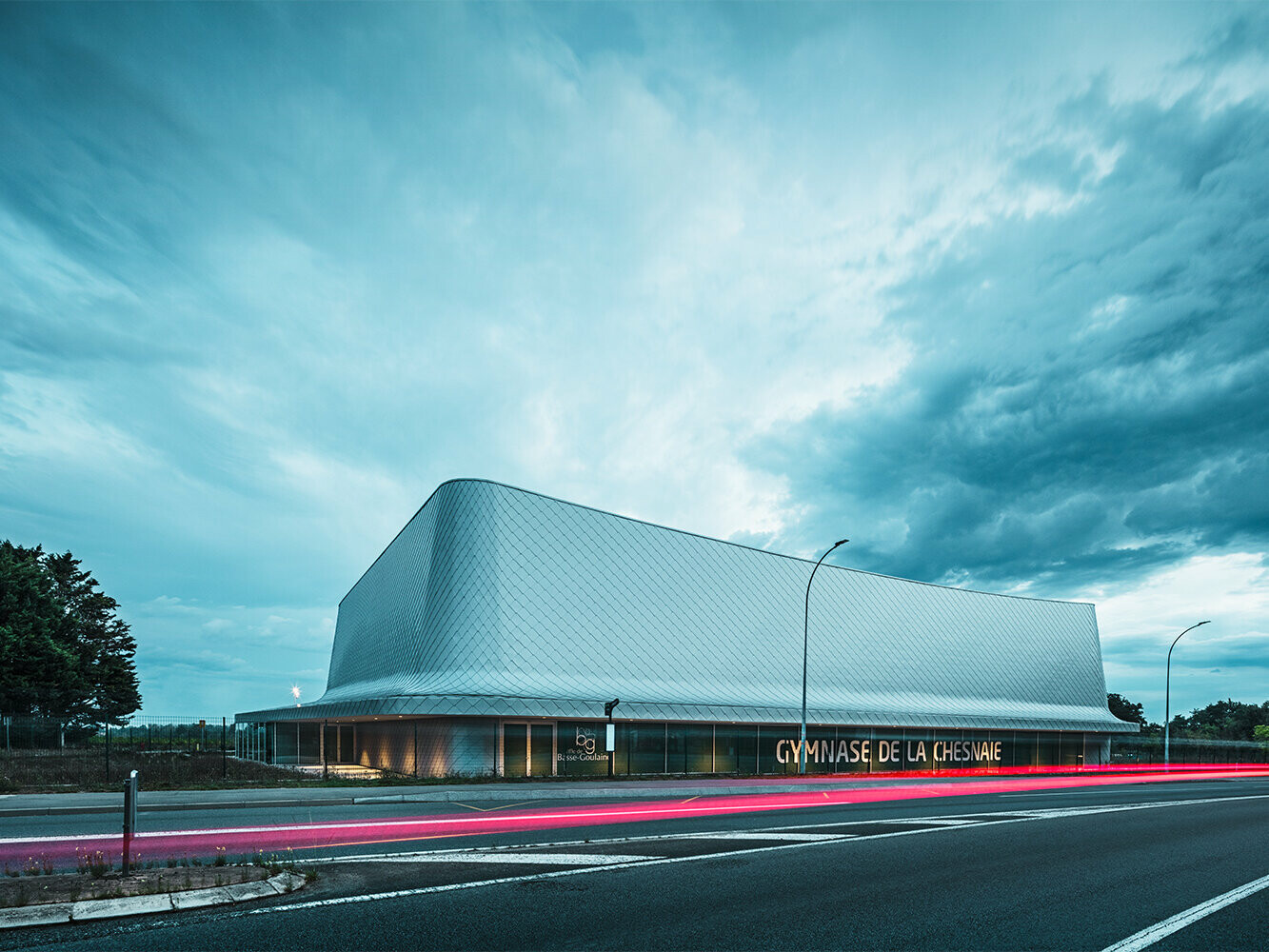 Ansicht der Sporthalle von der Straße aus mit bewölktem Himmel.