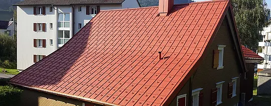 Saddeltag beklædt med PREFA tagplader af aluminium. Tag i teglstensrød med snestoppere og skorsten.