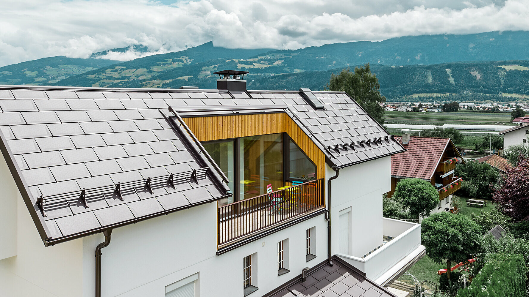 Boligbyggeri inddækket med aluminiumstagplade R.16 i nøddebrun af PREFA med stor altan og lys pudset facade.