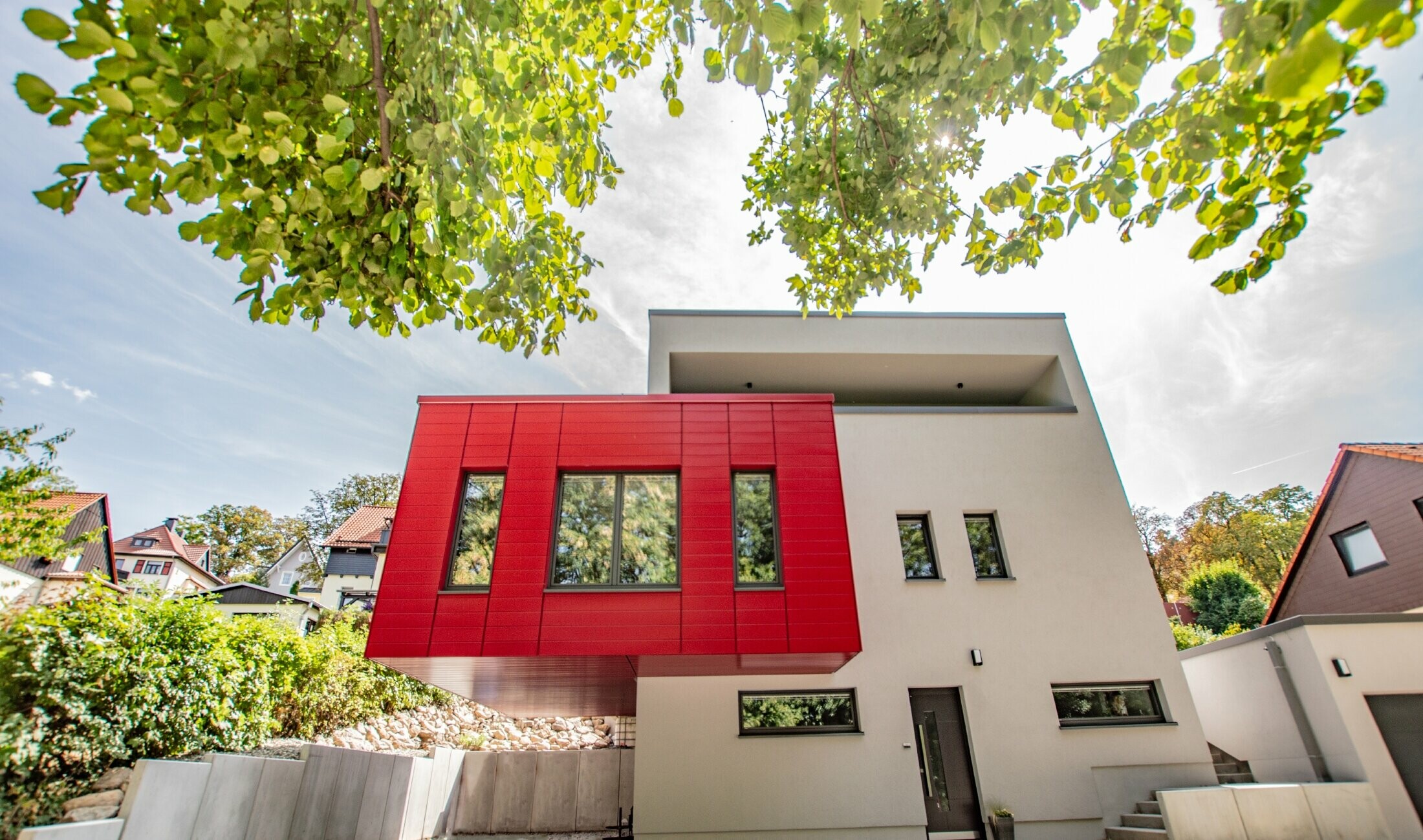Udhængende bygningsdel beklædt med PREFA Siding i rubinrød. Stor rød karnap, der løfter sig op fra den hvide facade.
